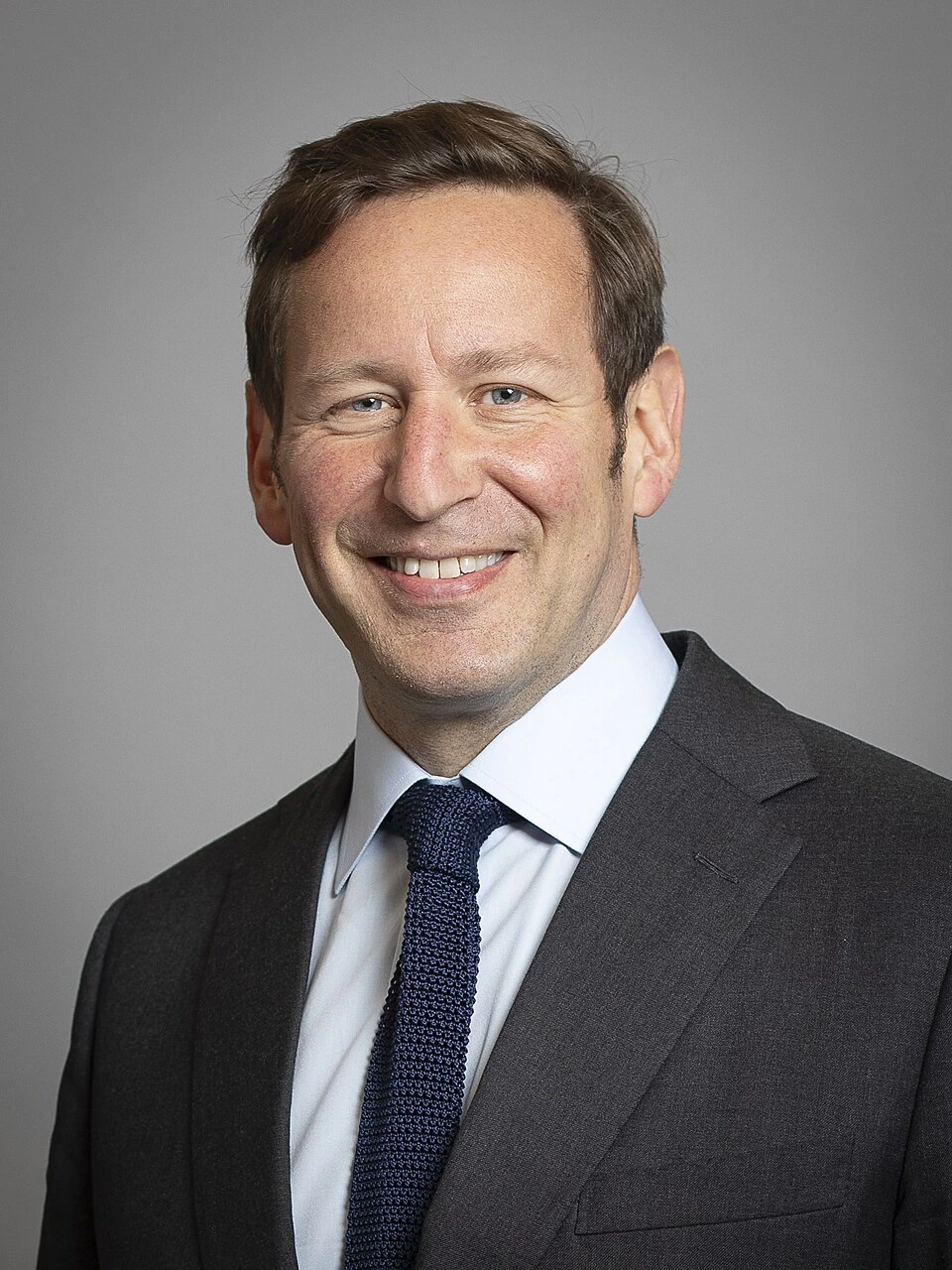 Official portrait of Ed Vaizey smiling in a suit and tie against a plain background