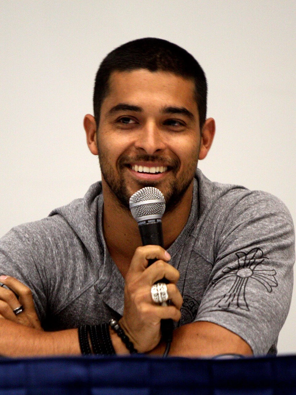 Wilmer Valderrama smiling while speaking into a microphone at a panel event.