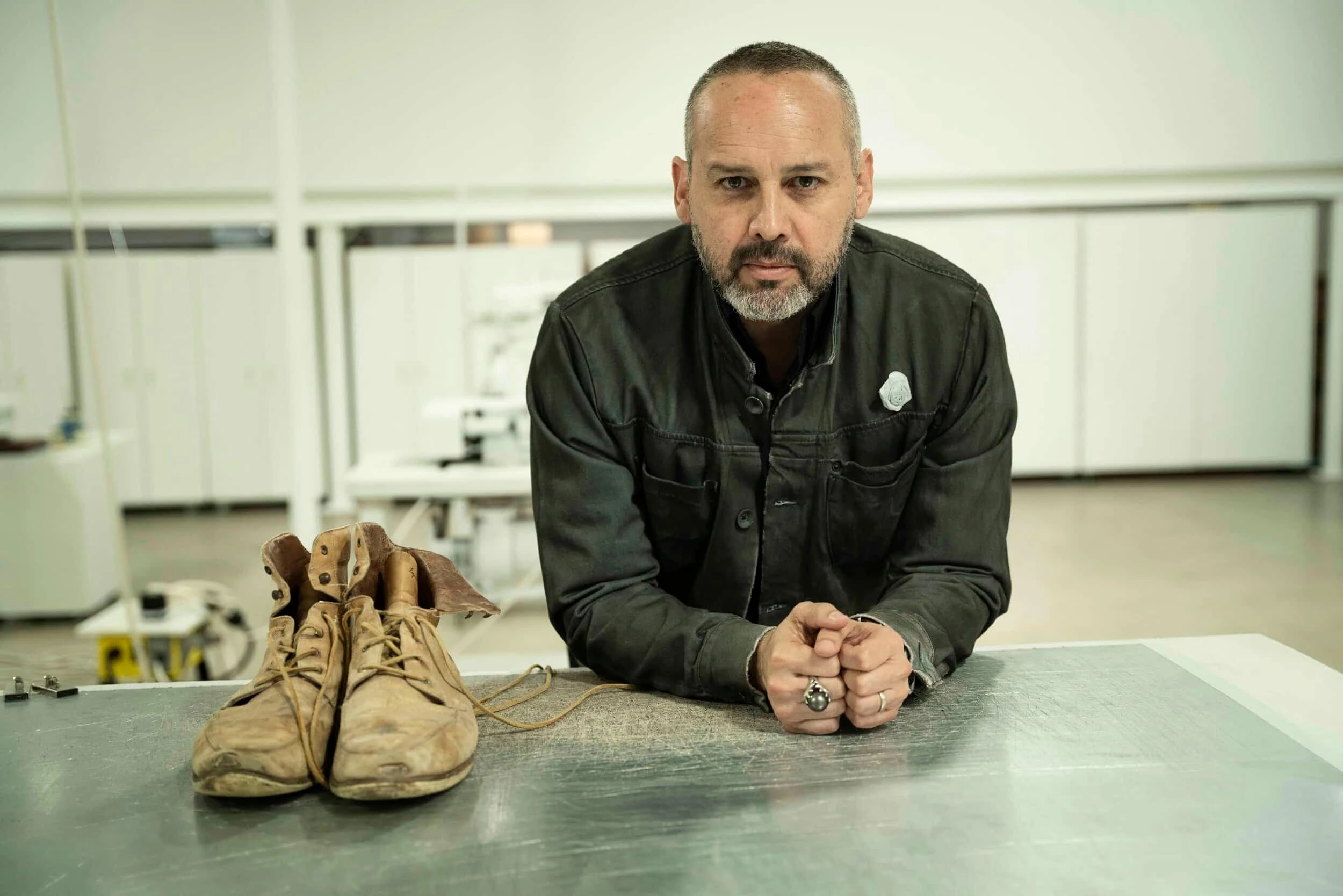 George Esquivel in his atelier, leaning over a worktable beside a pair of shoes